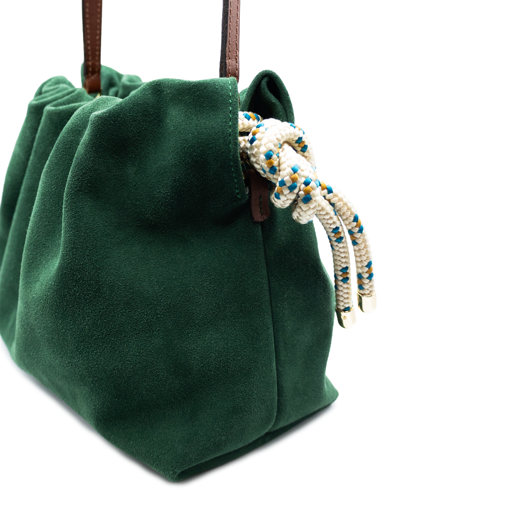 A dark green suede drawstring bag with brown leather straps and a knotted cream paracord rope accent featuring blue and gold check accent details, shown on a white background.