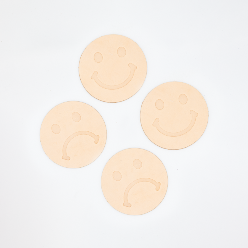 Set of 4 natural leather coasters stamped with frowny face and smiley faces